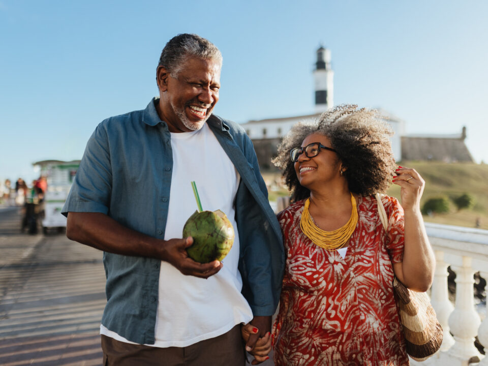 Carefree senior couple strolling and enjoying a holiday with a refreshing coconut drink under clear skies.